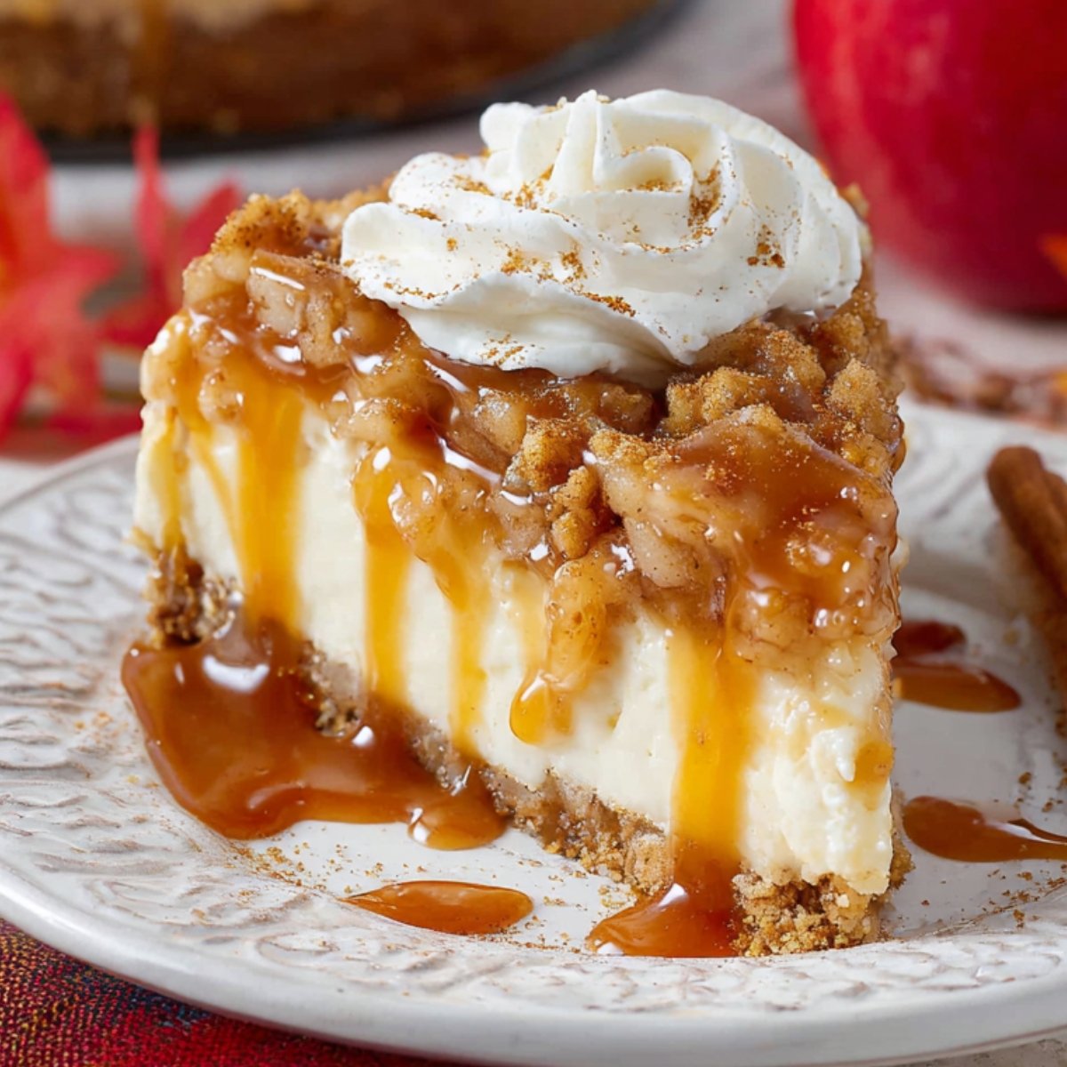 A slice of apple crisp cheesecake topped with whipped cream, caramel sauce, and cinnamon, showing a creamy interior with a graham cracker crust.