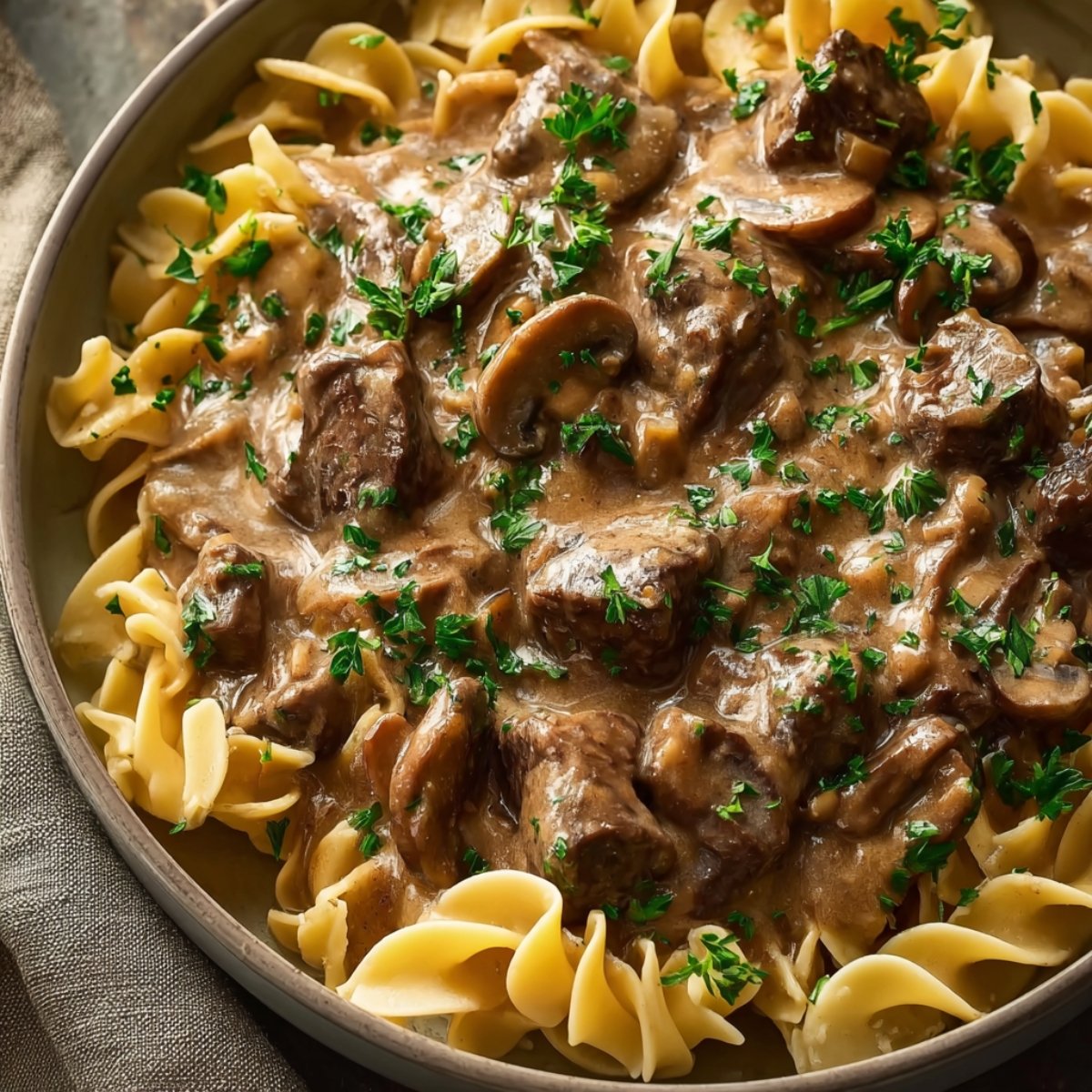 A plate of Beef Stroganoff served over egg noodles, garnished with fresh parsley and mushrooms, offering a rich and creamy texture.