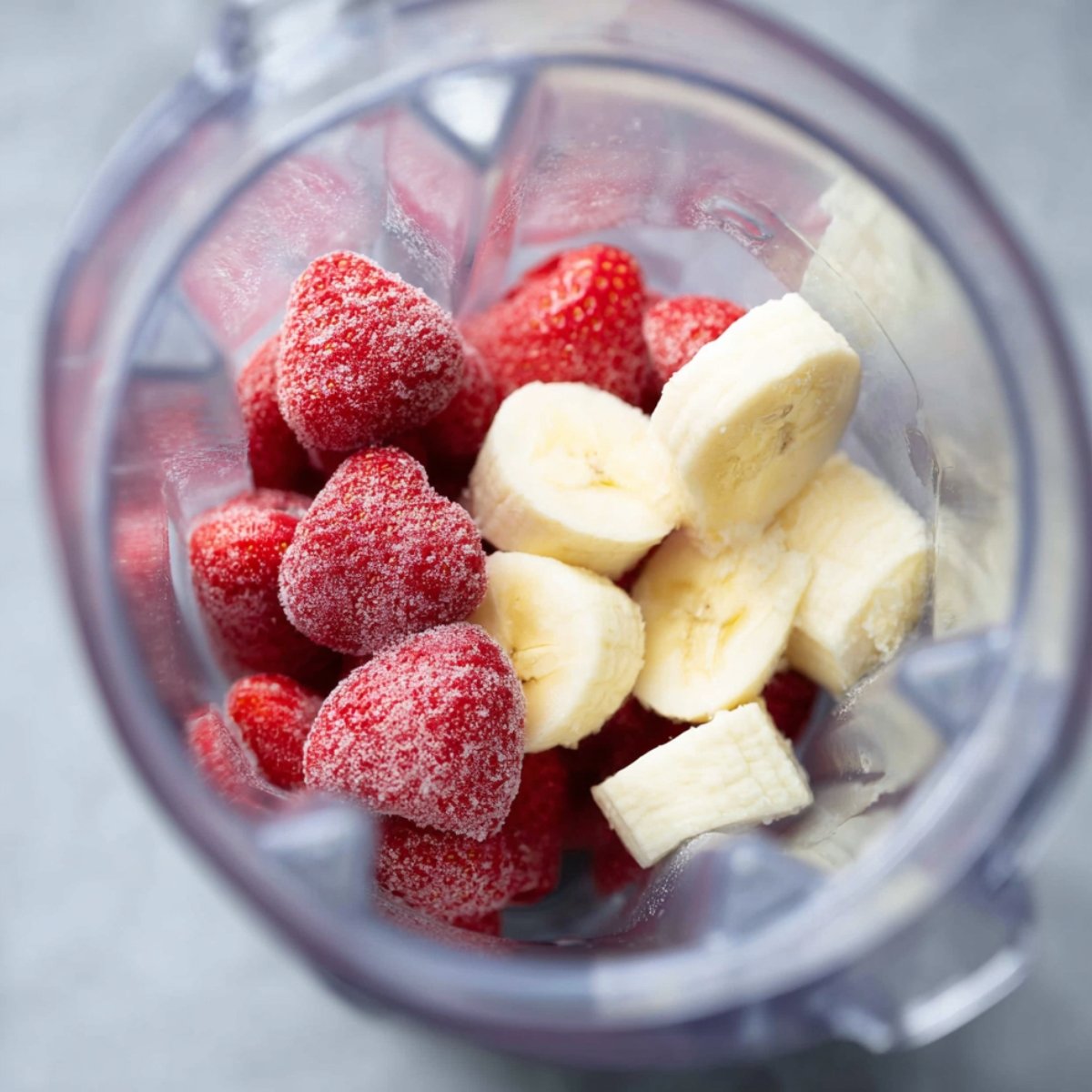 A blender containing frozen strawberries and sliced bananas, ready to be blended into a smoothie.