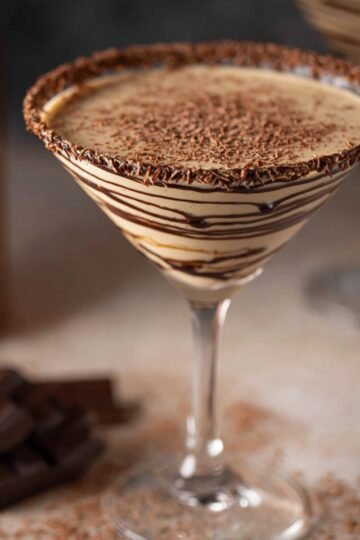 A finished chocolate martini with a beautifully decorated rim of chocolate drizzle and a sprinkle of grated chocolate, ready to be enjoyed.