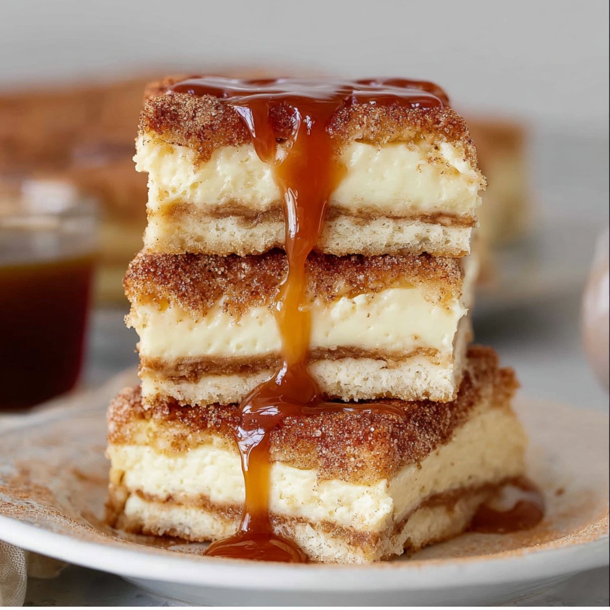 Sliced churro cheesecake bars stacked on a plate, with caramel sauce dripping down the sides, showcasing their creamy cheesecake filling and crispy cinnamon-sugar crust.