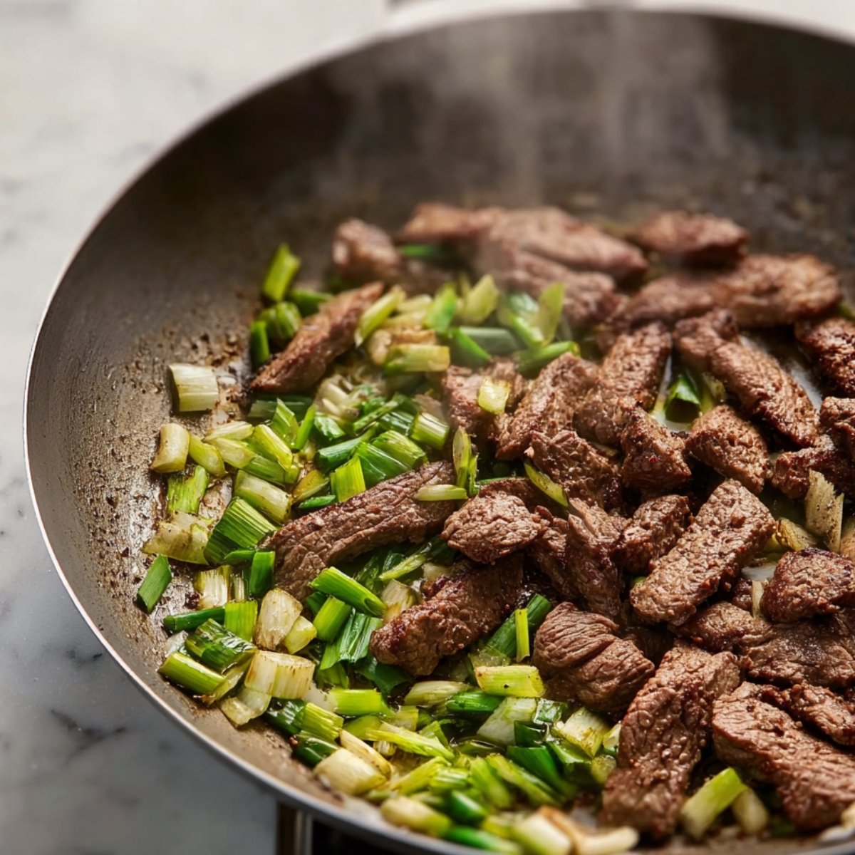 Beef strips cooking in a pan with sliced green onions, adding flavor and texture as the ingredients begin to soften.