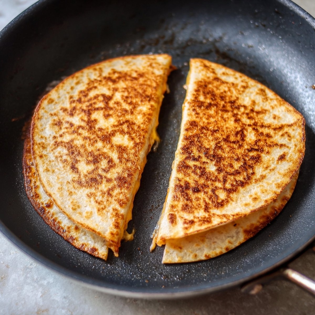 Golden-brown quesadilla halves in a skillet, with a crispy, perfectly toasted exterior, ready to be served.