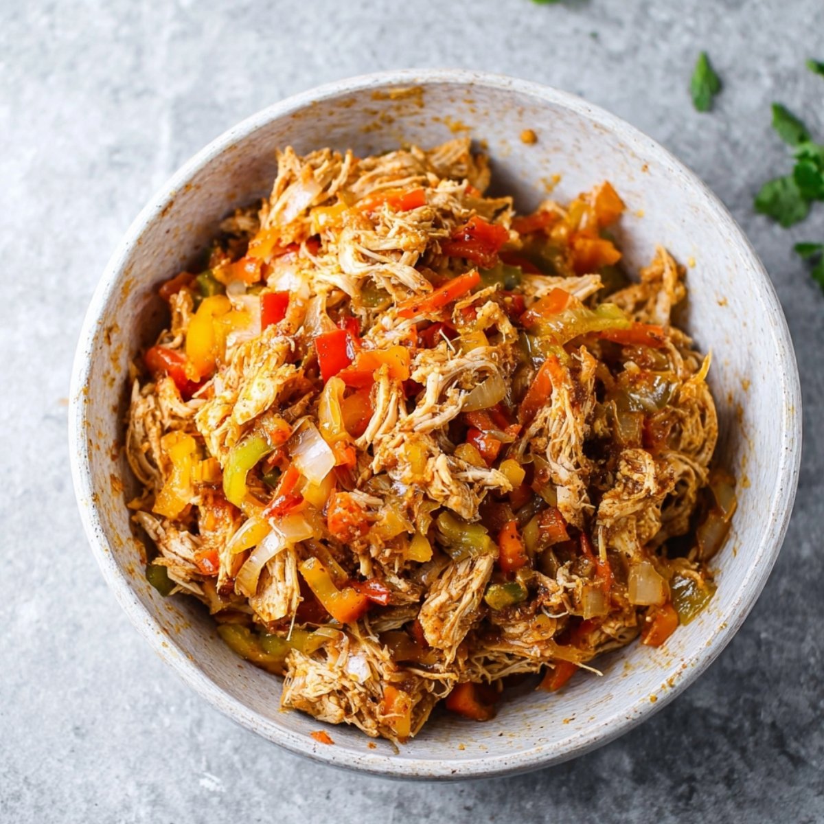 Bowl of seasoned shredded chicken mixed with diced peppers and onions, ready to be used as a filling for quesadillas or tacos.