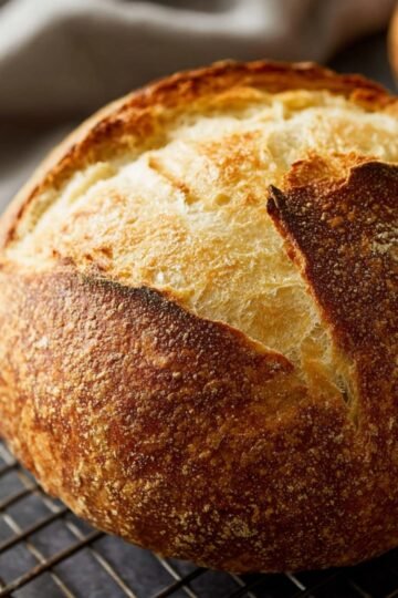 A golden-brown, perfectly baked round Homemade Sourdough Bread resting on a cooling rack, with a crisp, cracked crust.