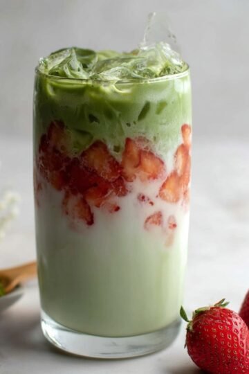 Layered Iced Strawberry Matcha Latte in a tall glass with milk, strawberry pieces, matcha, and ice cubes