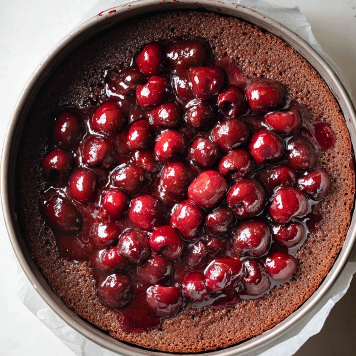 Chocolate cake layer topped with glossy cherry filling inside a springform pan.