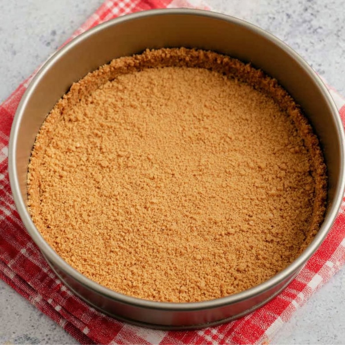 A graham cracker crust in a springform pan, evenly pressed into the bottom, ready for the cheesecake filling.