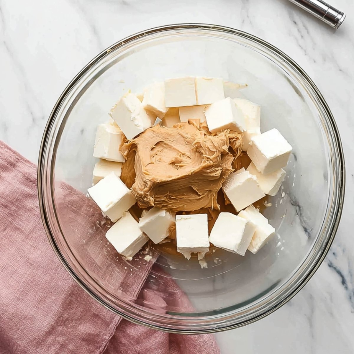 A glass mixing bowl containing cream cheese and peanut butter, with the ingredients awaiting to be blended together.