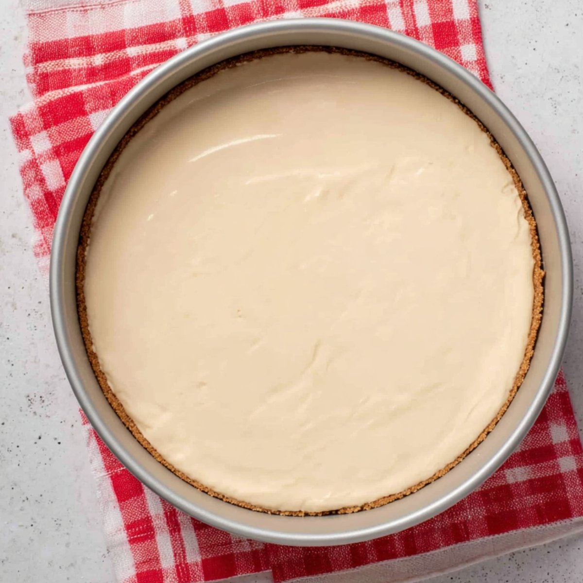 Smooth, creamy cheesecake batter poured into a springform pan, evenly spread over the graham cracker crust.