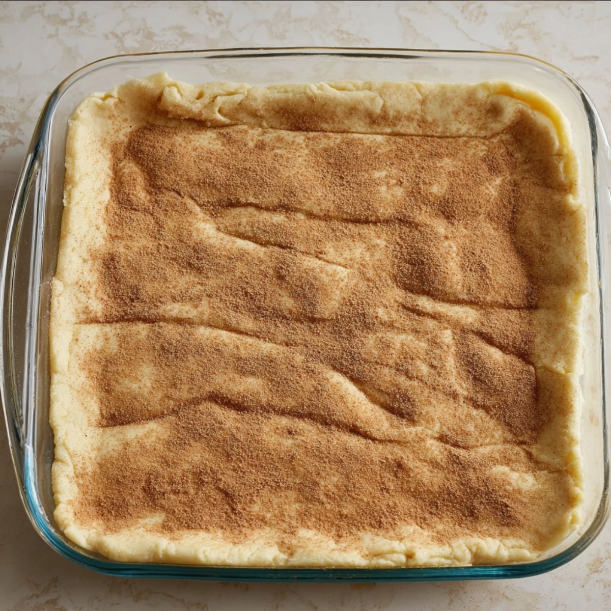 Crescent roll dough spread out in a glass baking dish, forming the base crust for a churro cheesecake dessert.