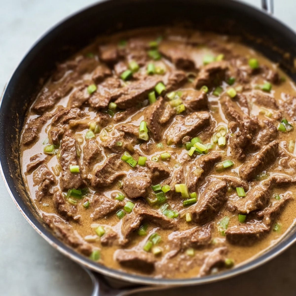 Beef strips simmering in a creamy sauce, topped with fresh green onions, creating a rich and savory Beef Stroganoff.