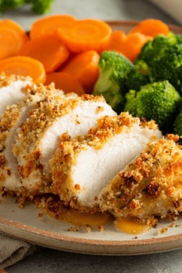 A close-up image of Baked Ranch Chicken, golden and crispy, served with steamed broccoli and sliced carrots on a plate. The chicken is perfectly cooked with a crunchy coating.