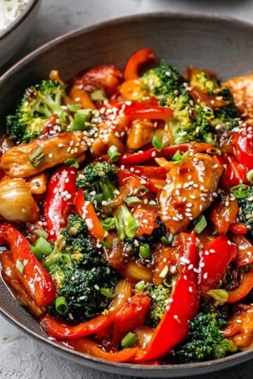 A bowl of vibrant Chicken Stir Fry featuring tender chicken, colorful vegetables, and a glossy sauce, garnished with sesame seeds and green onions.