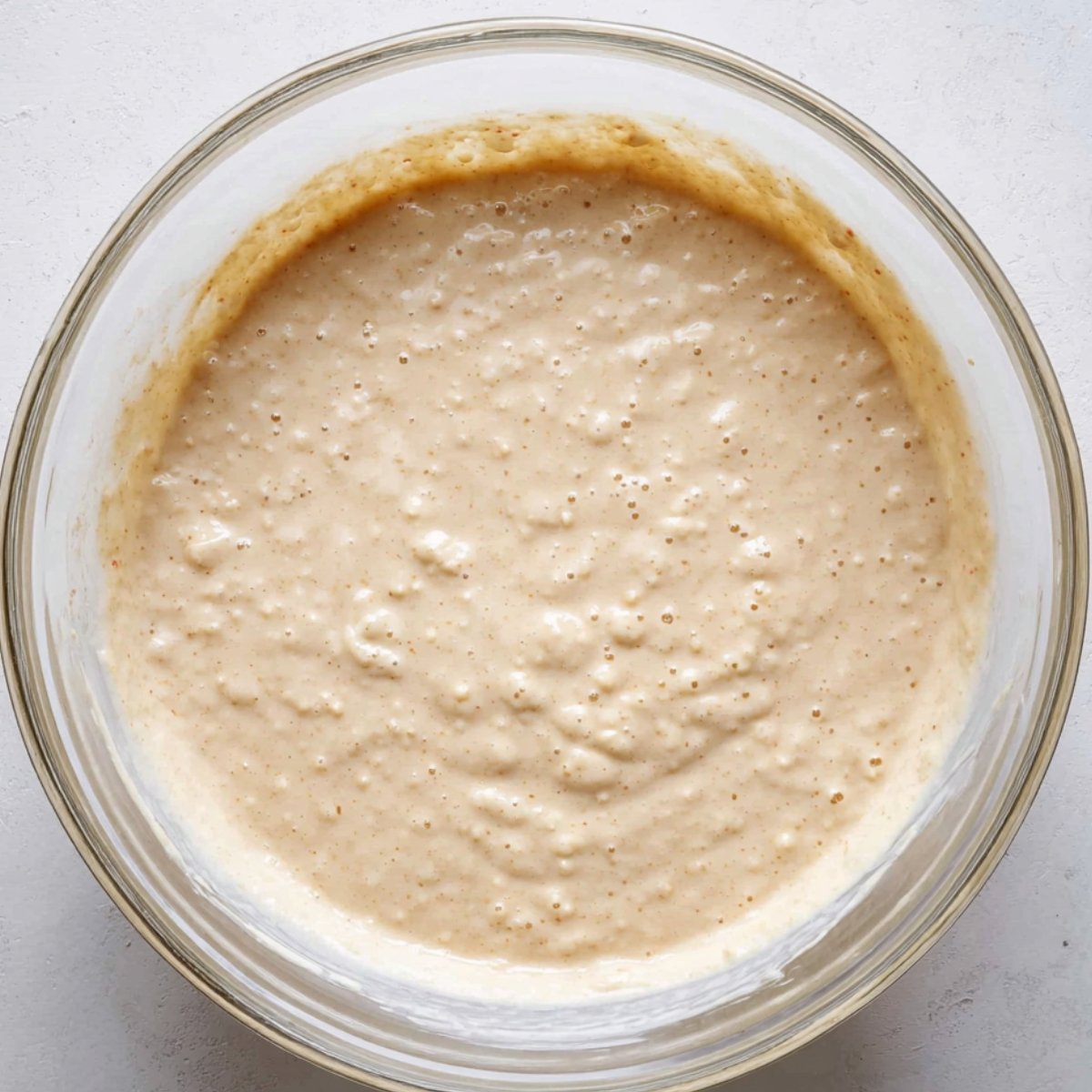 A glass mixing bowl filled with smooth pancake batter, showing small air bubbles, indicating the batter is ready to cook.
