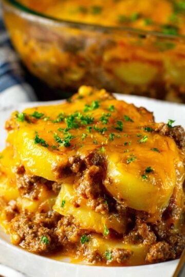 A delicious serving of Ground Beef and Potato Casserole, layered with seasoned ground beef, tender potatoes, and melted cheddar cheese, topped with fresh parsley for a burst of color.