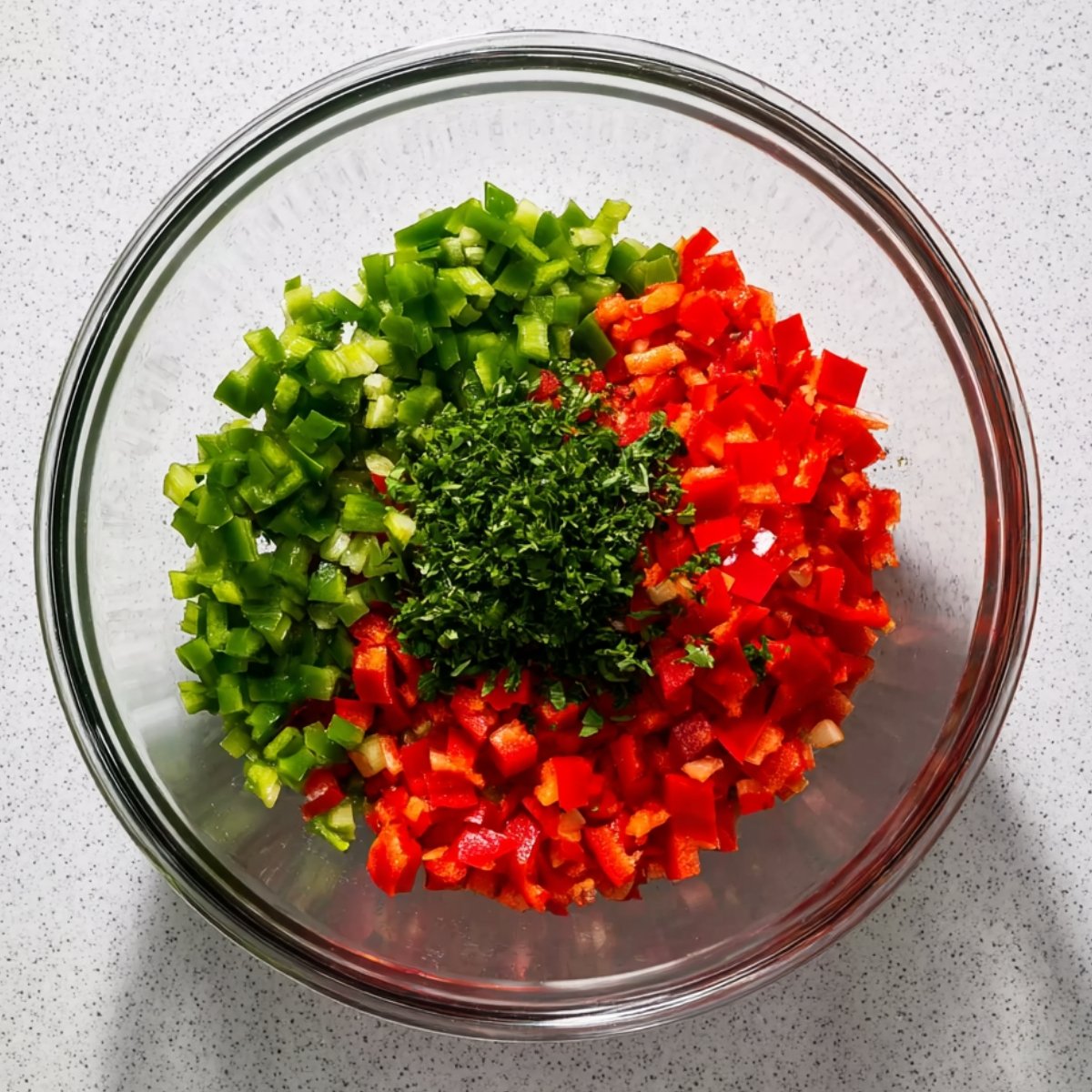 A bowl of chopped red bell peppers, green bell peppers, and fresh herbs for preparing egg muffins.