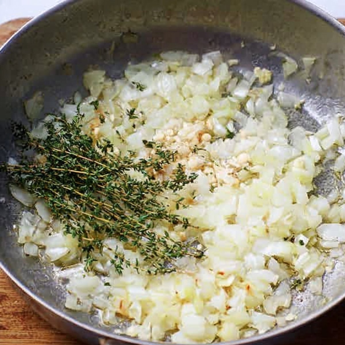 Onions, garlic, and fresh thyme are sautéed in oil to create a fragrant and savory base for the dish.