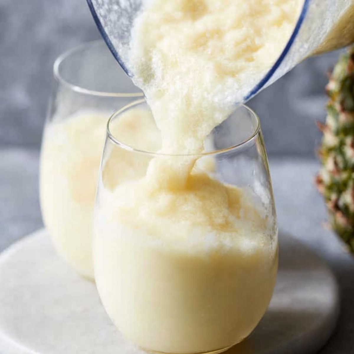 Pouring a creamy pina colada mixture from a blender into glasses, ready to be served.