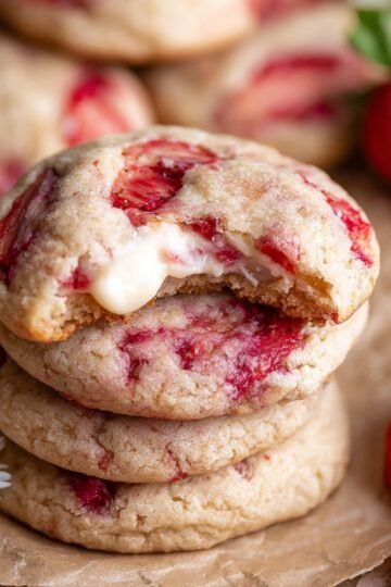 Stack of Strawberry Cheesecake Cookies with a bite taken out, revealing the creamy filling.